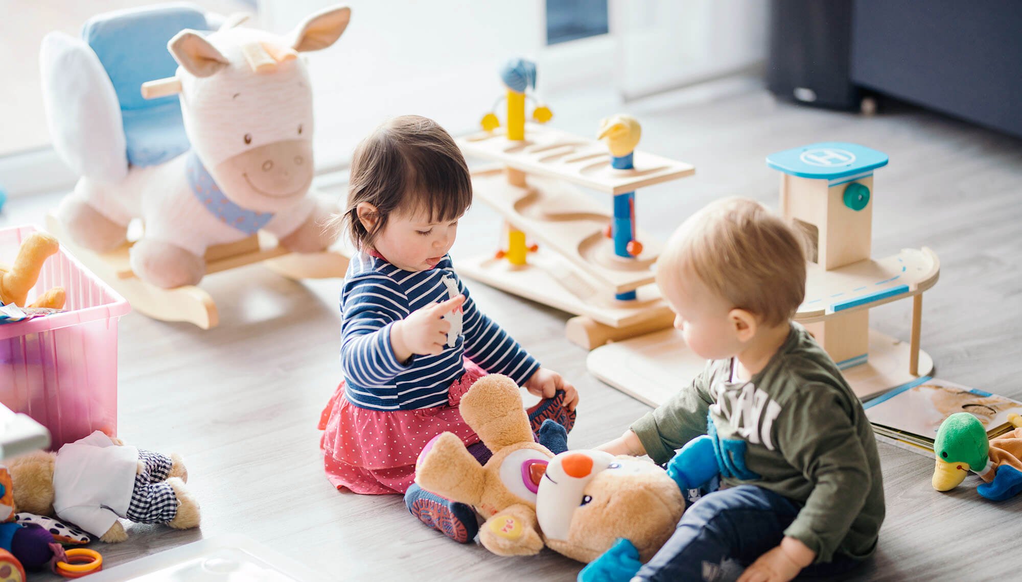 Dos niños juntos en el suelo rodeados de juguetes y peluches.