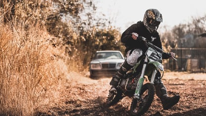 Un motociclista conduciendo fuera de la carretera por un camino de tierra, inclinándose en una curva, con un coche en el fondo.